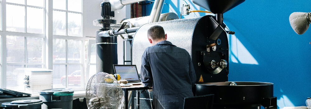 Ein Mann arbeitet an einem Laptop vor einer groen Industriemaschine in einer modern ausgestatteten Fabrikumgebung.